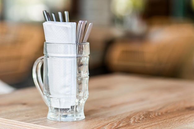 Cutlery and white napkins in a beer mug on a table in a street cafe