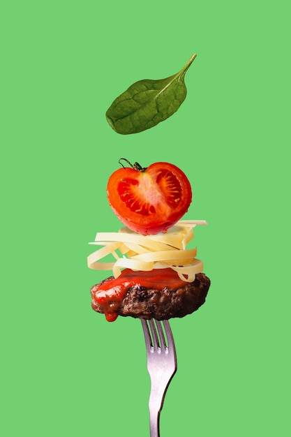 Cutlet, pasta, tomatoes, spinach strung on a fork on a green background