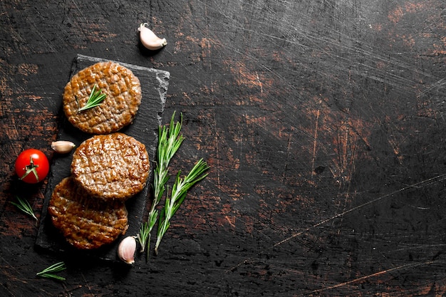 Cutlets on a black stone Board with pieces of garlicrosemary and cherry