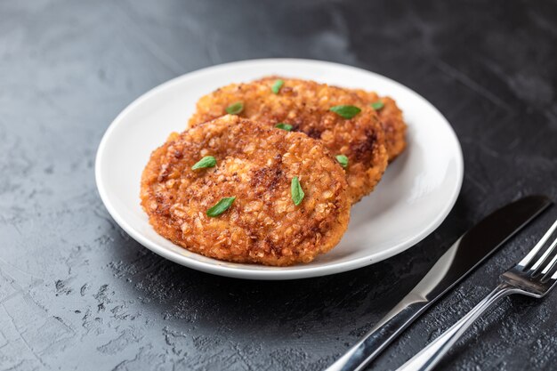 Cutlets lie on a white plate. Chicken cutlets lie among the vegetables on a black stone table.