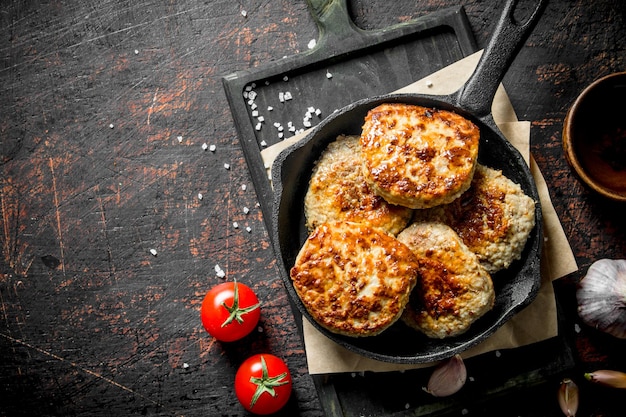 Cutlets in the pan on the paper with garlic and tomatoes