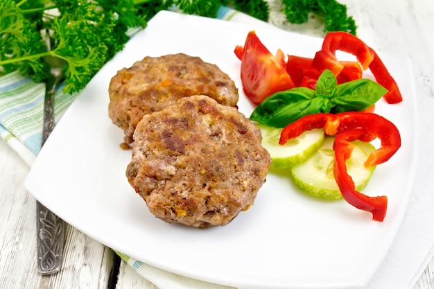 Cutlets stuffed with spinach and eggs in a dish, a salad of tomatoes, cucumber and pepper, basil and parsley on a wooden board background