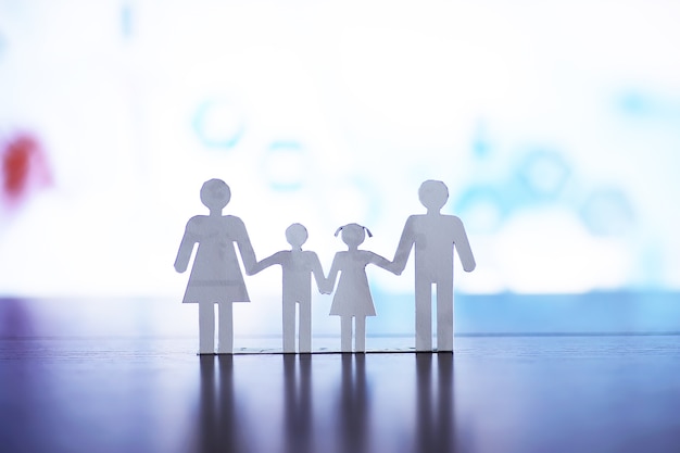 cutout paper chain family with the protection of cupped hands, concept for security and care. hands with cut out paper silhouette on table. family care concept