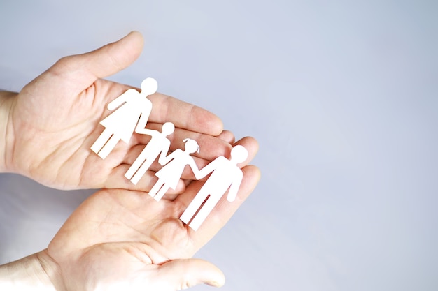 Cutout paper chain family with the protection of cupped hands, concept for security and care. Hands with cut out paper silhouette on table. Family care concept