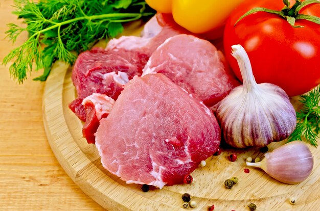 Cuts of meat, garlic, tomato, pepper pots of different, parsley and dill on a wooden board