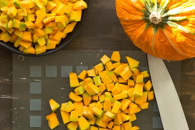 Photo cutted pieces of pumpkin on glass cutting board on the wooden background