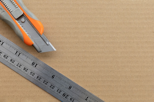 Cutter knives and steel ruler on paper crates background. top view