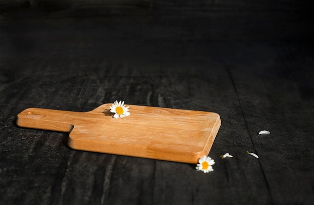 cutting board lies on a black surface with chamomile flowers