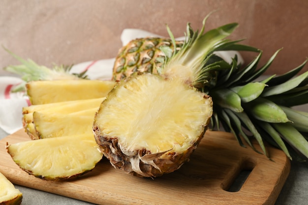 Cutting board and pineapples on grey background, close up