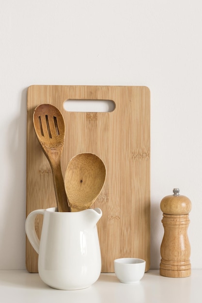 Cutting board, spoons and spice mill on table wall background.