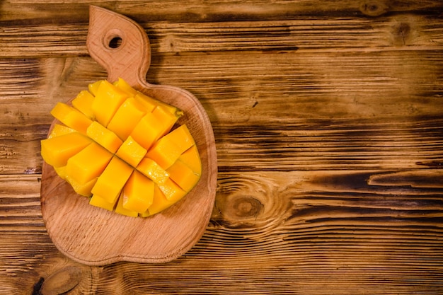 Cutting board with chopped mango fruit on rustic wooden table. Top view
