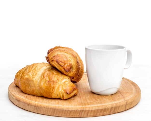 Foto tagliere con una tazza di caffè e due croissant sul tavolo isolato su bianco