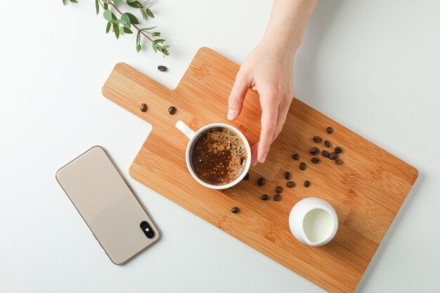 Cutting board with cup of fresh coffee, milk coffee beans, phone, female hands