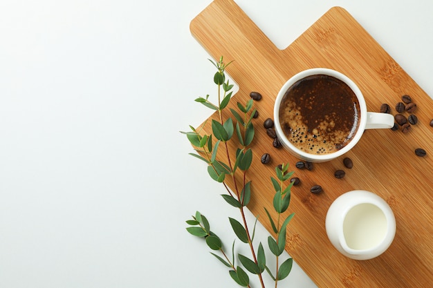 Cutting board with cup of fresh coffee milk, coffee beans and plant branch on white background