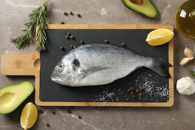 Cutting board with Dorado fish and cooking ingredients on grey background, top view