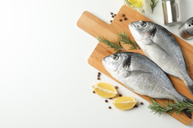 Cutting board with Dorado fishes and cooking ingredients on white background, top view