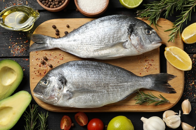 Cutting board with Dorado fishes and cooking ingredients on wooden background