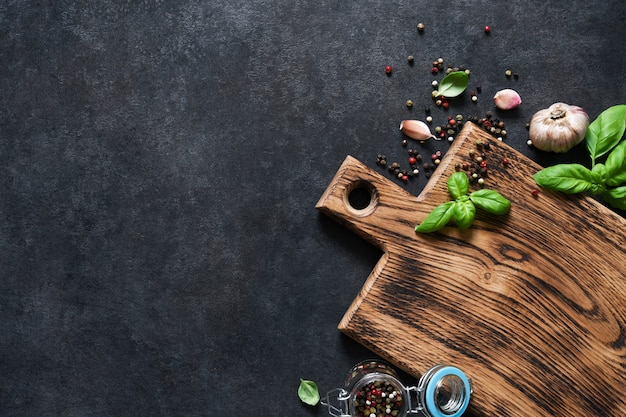 Cutting board with fresh basil and spices on a black concrete table. Top view with copy space.