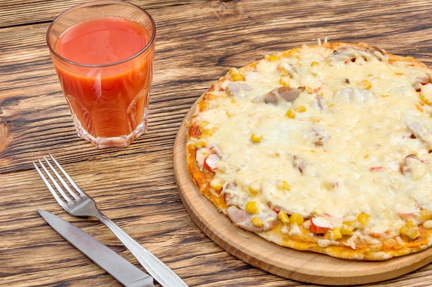 Cutting board with fresh pizza and glass of tomato juice on the wooden table