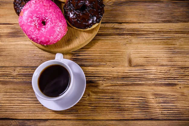 Cutting board with glazed donuts and cup of coffee on a wooden table. Top view