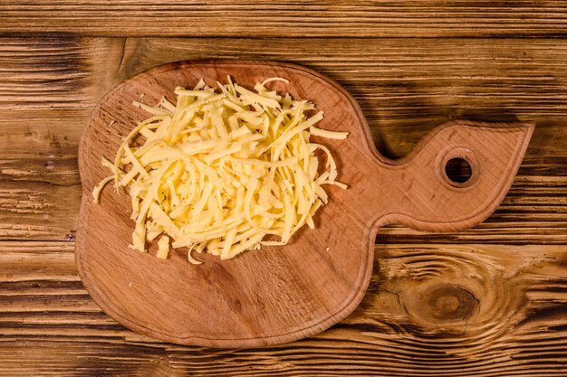 Cutting board with grated cheese on rustic wooden table. Top view