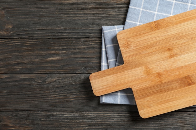 Cutting board with kitchen towel on wooden background, space for text
