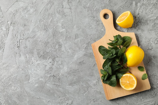 Cutting board with lemon and mint on grey, space for text