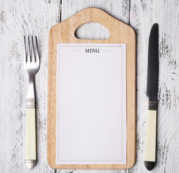 Cutting board with menu sheet of paper on color wooden background