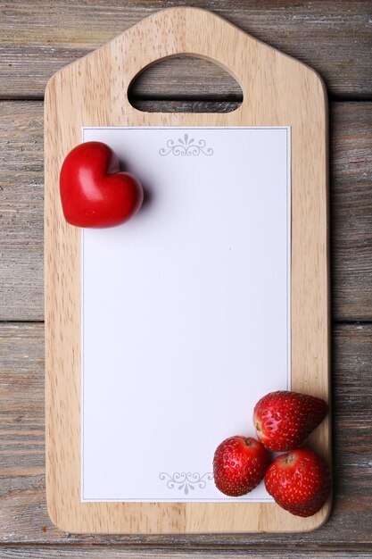 Photo cutting board with menu sheet of paper, heart and strawberry on rustic wooden planks background