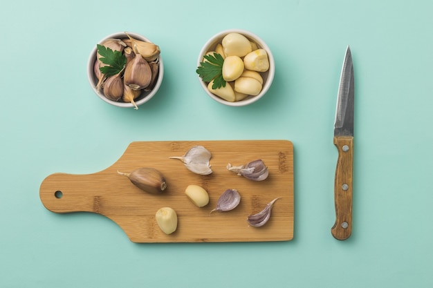 Cutting board with peeled and unpeeled garlic and a knife on a blue surface