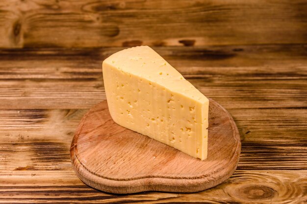 Cutting board with piece of cheese on rustic wooden table