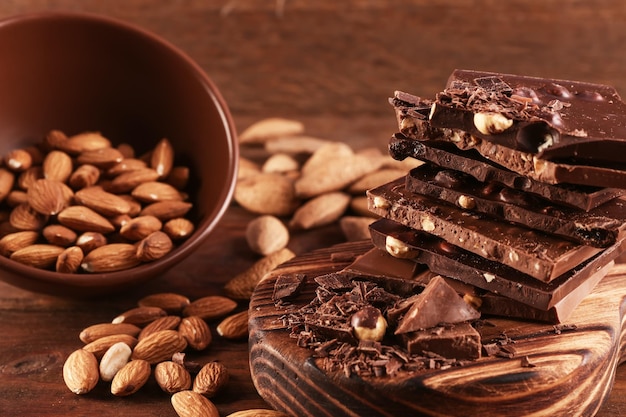 Cutting board with pile of chocolate bowl and nuts on wooden background