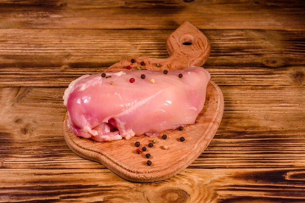 Cutting board with raw chicken fillet and different spices on rustic wooden table