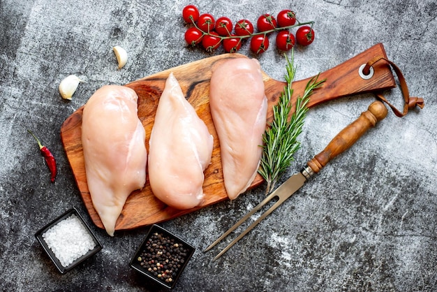 A cutting board with raw chicken on it and a knife next to it.