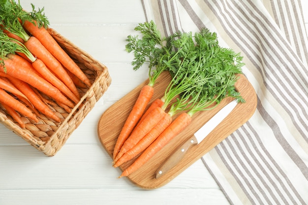 Cutting board with ripe carrots and knife on wooden table