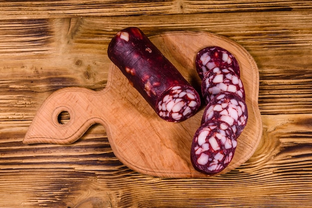 Cutting board with sliced salami sausage on rustic wooden table. Top view