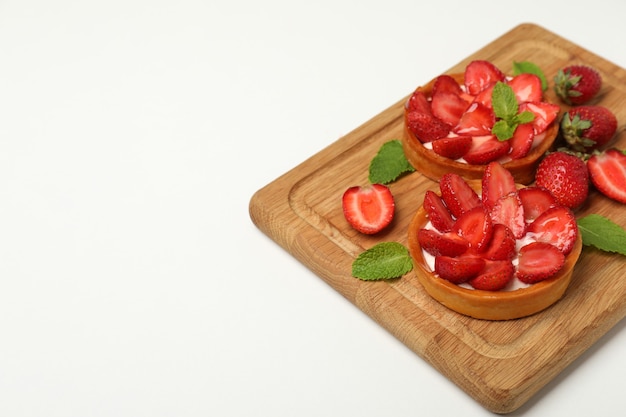 Cutting board with strawberry tarts on white background.