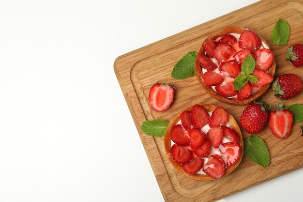 Cutting board with strawberry tarts on white background.