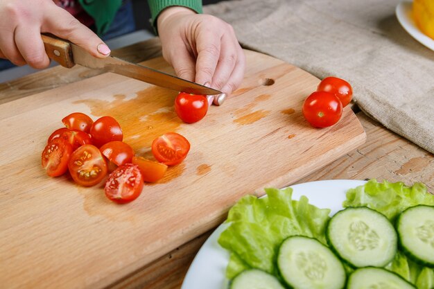 まな板の上で、女性はチェリートマトのレジームを野菜サラダ用のスライスにナイフで切ります。正面図