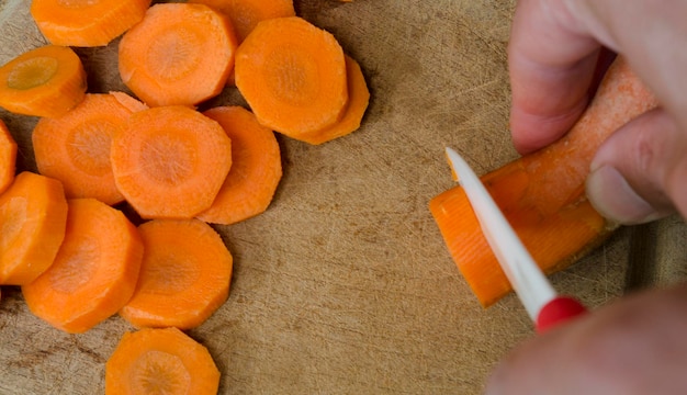 Cutting carrots top view with ceramic knife on wooden plate