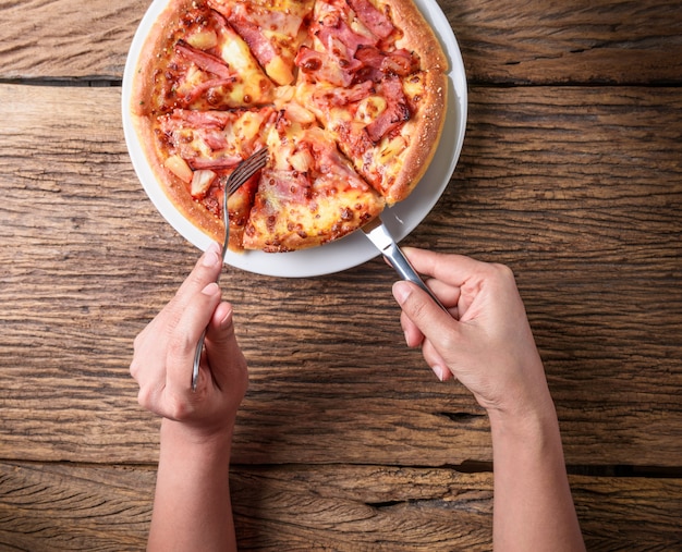 Foto tagliare una deliziosa pizza italiana con formaggio, funghi, carciofi e pomodori con l'aiuto del coltello