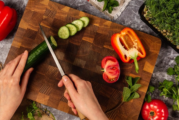 Cutting fresh cucumber on wooden cutting board with knife