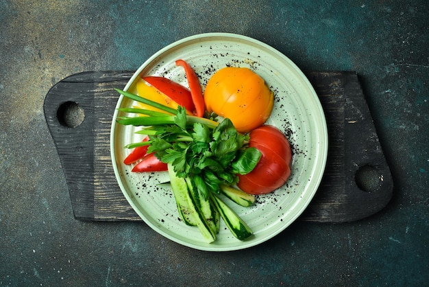 Foto taglio di verdure fresche pomodori paprika prezzemolo cilantro cipolle su un piatto su uno sfondo di pietra scura