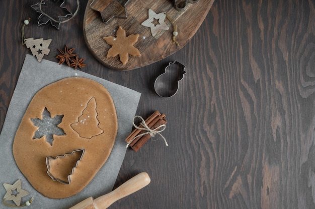 Cutting of gingerbread cookies from savory pastry dough with cutters on dark wooden table with anise