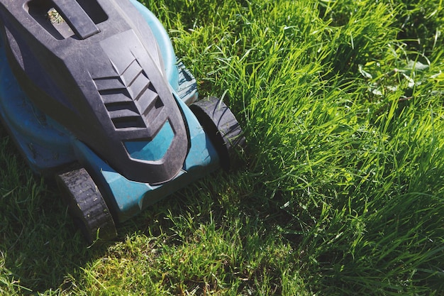 Cutting green grass electric lawn mower. The difference between the processed and overgrown parts of the field.