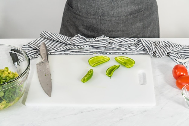 Cutting ingredients on a white cutting board to make classic guacamole dip.