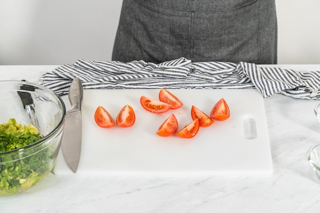 Cutting ingredients on a white cutting board to make classic guacamole dip.