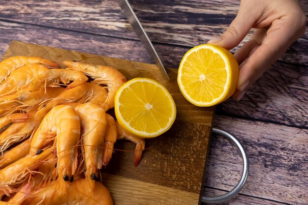 Cutting a lemon near boiled shrimp on a wooden stand