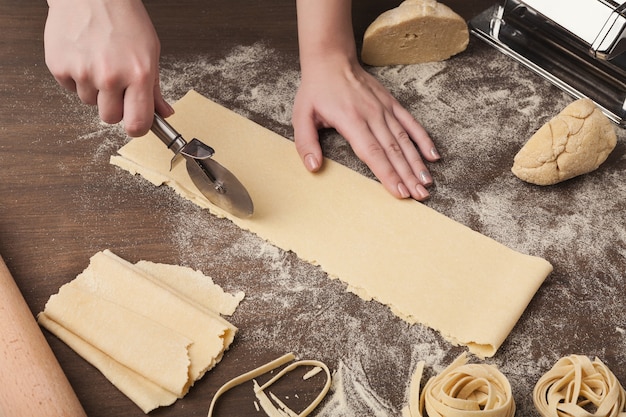 Cutting raw dough. Chef using wheel cutter in preparation of italian pasta on kitchen table, copy space