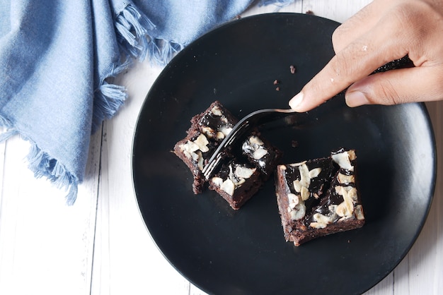 Cutting slice of brownie with fork on plate on table